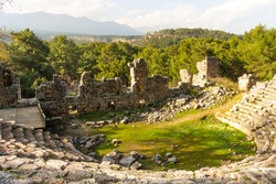 Ruins of the amphitheatre of the ancient ancient city of Phaselis illuminated by the bright sun in sunny weather on mountains and clouds background in Turkey, Antalya, Kemer. Turkey national landmarks