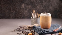 Latte or cappuccino with milk foam and lavender in a glass with coffee beans. Dark background