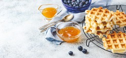 Traditional belgian homemade waffles with blueberry, honey and orange jam on metal grid on light background. Long wide banner