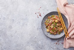 Wok with turkey meat, soba noodles, corn, green peas, green beans and carrots served on gray background with chopsticks. Asian food, concept of street food. Top view with copy space