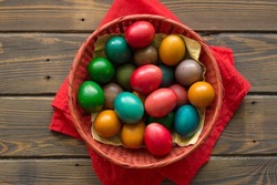 Top view of Easter colored eggs in a red wicker basket at red handkerchief on a table of wooden planks