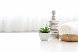 Ceramic soap, shampoo bottles and white cotton towels on white counter table inside a bright bathroom background.