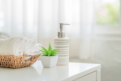 Ceramic soap, shampoo bottles and white cotton towels with green plant on white counter table inside a bright bathroom background