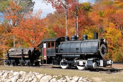 Colorful fall foliage and historic steam-powered Porter Locomotive coupled to old freight car. Used for hauling logs harvested in White Mountains of New Hampshire.