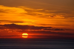 The orange setting sun in the clouds over the dark sea.