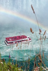 Niagara falls in Canada with green grass and flowers on the foreground, Ontario. Tourist boat sails to the waterfall. A rainbow over a blue water.