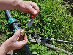 installation of a garden metal faucet on a plastic pipe, assembly by male hands of parts of a garden irrigation system against the background of green grass and a lying gas key
