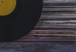 A stack of old vinyl records stacked on top of each other in multi-colored covers, on the side is a black vinyl record with a yellow blank label for text. Jazz vinyl record listening concept.