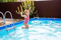 Cute little girl preparing to jump into blue water, having fun in the pool, fine swimmingpool at home, summer time in daycare, holiday and vacation concept .