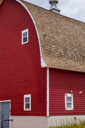Red barn with white windows and cement foundation.  Pale sky over the side of a red barn with tan roof.  Colorado barn with windows on the front and side.  