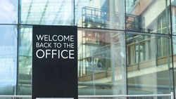 Welcome back to the office on a city-center sign in front of a modern office building	