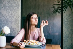 Pretty young lady sitting in a beautiful restaurant, enjoying lunch or dinner and making delicious hand gesture to express how good the food is. 