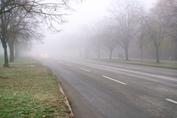 Car approaching with lights on on a city road. Fog, bad weather, reduced visibility. 