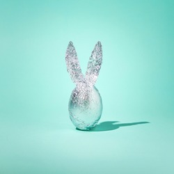 2022 Easter minimal concept. Egg in aluminium foil with rabbit ears and shadow on blue green background. Unique spring holiday idea. 