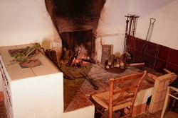 An old open fire and stove in a Tuscan country house. There is a chair in front of the fire.