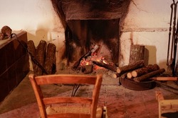 An open fireplace with a glowing fire, in front of it is an old wooden chair.
