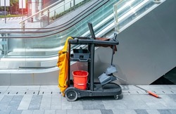 Cleaner cart in a public place with cleaning products: mop, buckets for cleaning the floor, broom scoop, household chemicals, household rags