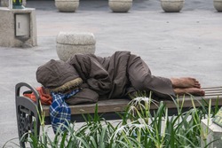 A homeless is sleeping on park bench.