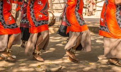 Traditional African dancers on sandals dance outdoors in brightly colored clothing. They are accompanied by drums and singing