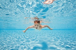 Happy young boy swim and dive underwater, kid breast stroke with fun in pool. Active healthy lifestyle, water sport activity and lessons with parents on summer family vacation with child.