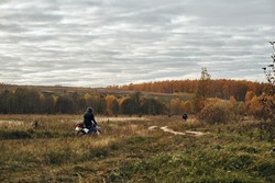 Autumn, motorcycle rides on rough terrain, motorcycles. Autumn landscape, on the horizon fields and forests are adjacent to the sky with clouds, on a dirt road rides a motorcyclist.