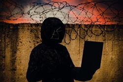 A hacker stands against the wall of a prison with barbed wire. Cybersecurity. Prison