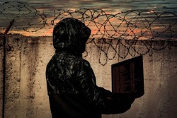 A hacker stands against the wall of a prison with barbed wire. Cybersecurity. Prison