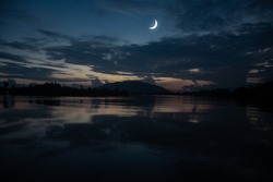 Concept the crescent moon the symbol of Islam begins the eid al Fitr. Seeing the moon in the night sky. The evening sky and the vast river in darkness are beautiful.