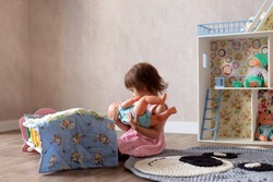 Cute little girl is playing with a doll at home. The child puts the doll to sleep in a toy bed. Role-playing games for children