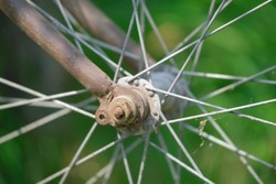 close up of rusty hub and rim spokes of an old metal bicycle wheel on background of green plants outdoor