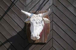 White sculpture of the head of bull hangs on a wall of wooden planks