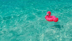 Pink, inflatable beach flamingo on the background of turquoise water. Hit of the summer