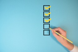Yellow marking on checklist box isolated on blue background. Checklist concept. Hand holding a pencil and checklist isolated on pastel blue background with copy space.
