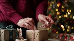 Woman in a burgundy sweater packs a lot of boxes with gifts in beautiful paper and ribbons, bows on the background of a Christmas tree.Preparing for Christmas,New Year holidays,gift wrapping.