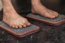 A woman stands with bare feet on a sadhu board with nails.Practice of standing on nails.Relaxation and meditation,alternative medicine.Close up,selective focus.