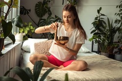 Young woman sitting in a lotus position at home and using singing bowl.Relaxation and meditation.Sound therapy,alternative medicine.Buddhist healing practices.Clearing the space of negative energy.
