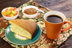 A cup of coffee with cake, candy, candied fruits and jam on a wooden table.
