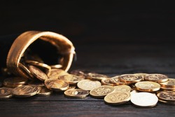 A bag with gold coins on a wooden background. The money is in a black bag. Treasure Hunt.Copy space. Place for text