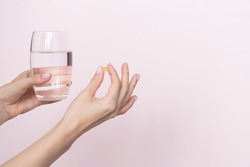 Woman holding pill and glass of water in hands taking emergency medicine, supplements or antibiotic antidepressant painkiller medication to relieve pain, meds side effects concept, close up view. 