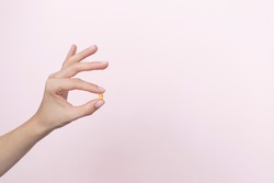 Woman hand holding yellow pill capsule on a pink background, medication concept with copy space. High quality photo