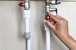 A woman's hand opens or closes a red water valve on a water pipe. Saving Water Consumption Concept