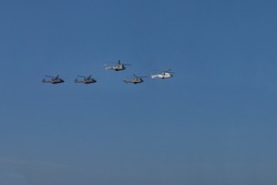 Group of helicopters specialized in war missions flying in formation during an exhibition of the air force with the blue sky as background.