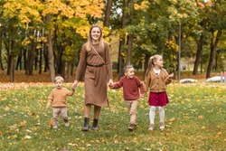 Mother and three children are having fun on an autumn day in the city park. The adorable boy his mom is holding. The older sister and brother hug their mother and younger brother. Big family. Children