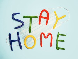 Stay home plasticine colorful letters. Light blue background with surgical facial mask. Stay home text in multi colored letters. Coronavirus, lockdown, safety concept. Kids, child worry about virus