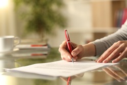 Close up of woman hands signing document with pen on a desk at home