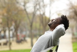 Side view portrait of a happy black man relaxing sitting on a bench in a park