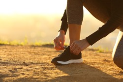 Closeup of runner woman hands tying shoelaces of shoes on the ground at sunset
