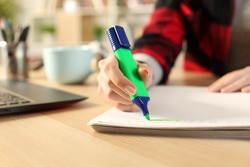 Close up of student girl hands using green highlighter pen on notebook on a desk at home