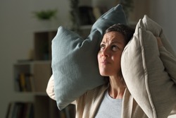 Annoyed adult woman suffering neighbour noise in the livingroom at night at home