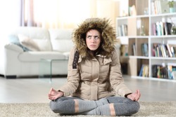 Front view portrait of an angry woman with damaged heater at home trying to relax doing yoga exercise